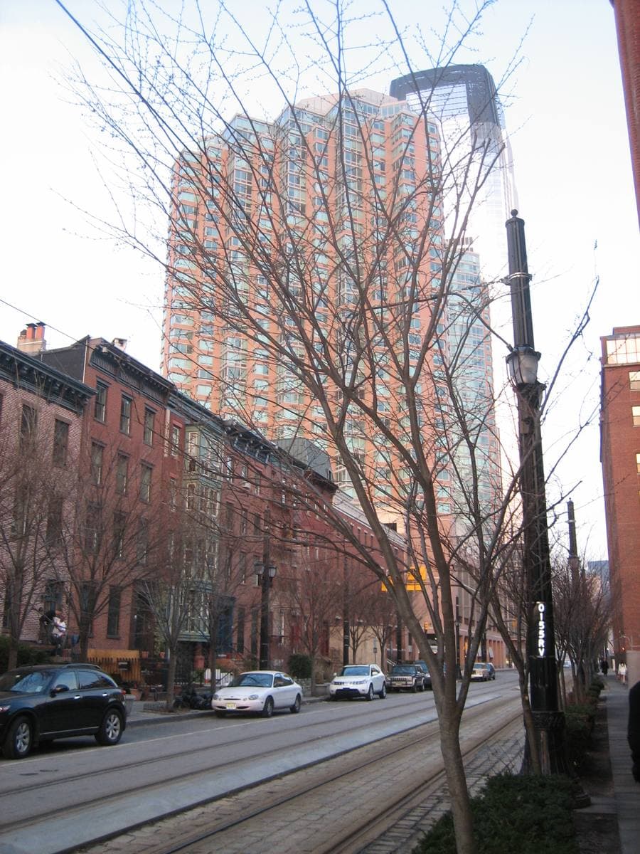 Brick row houses along a street with light-rail tracks and a glass tower behind