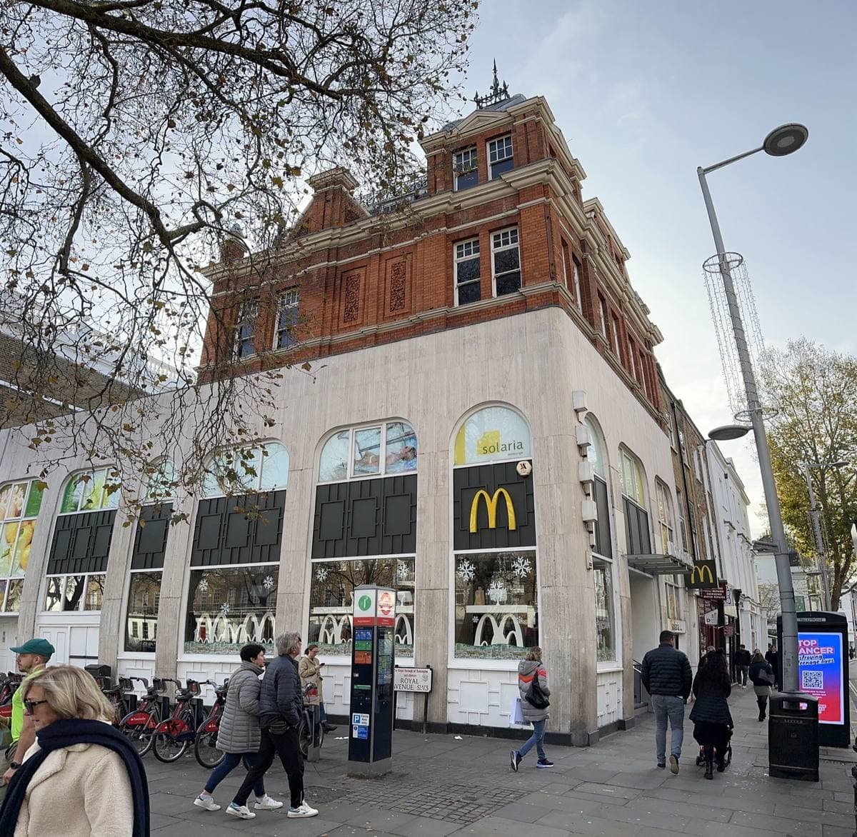 A pale stone corner shopfront with arched windows under a red-brick Victorian upper floor