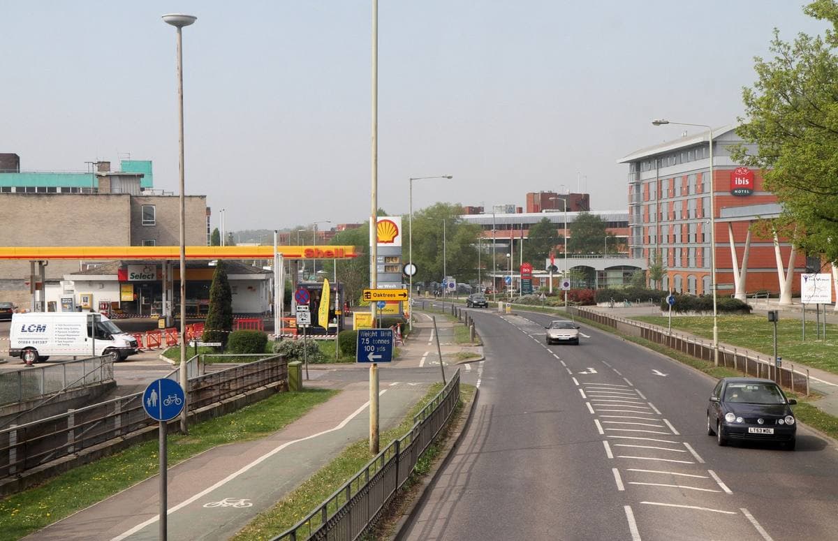 A wide road curving past a petrol station canopy and office blocks