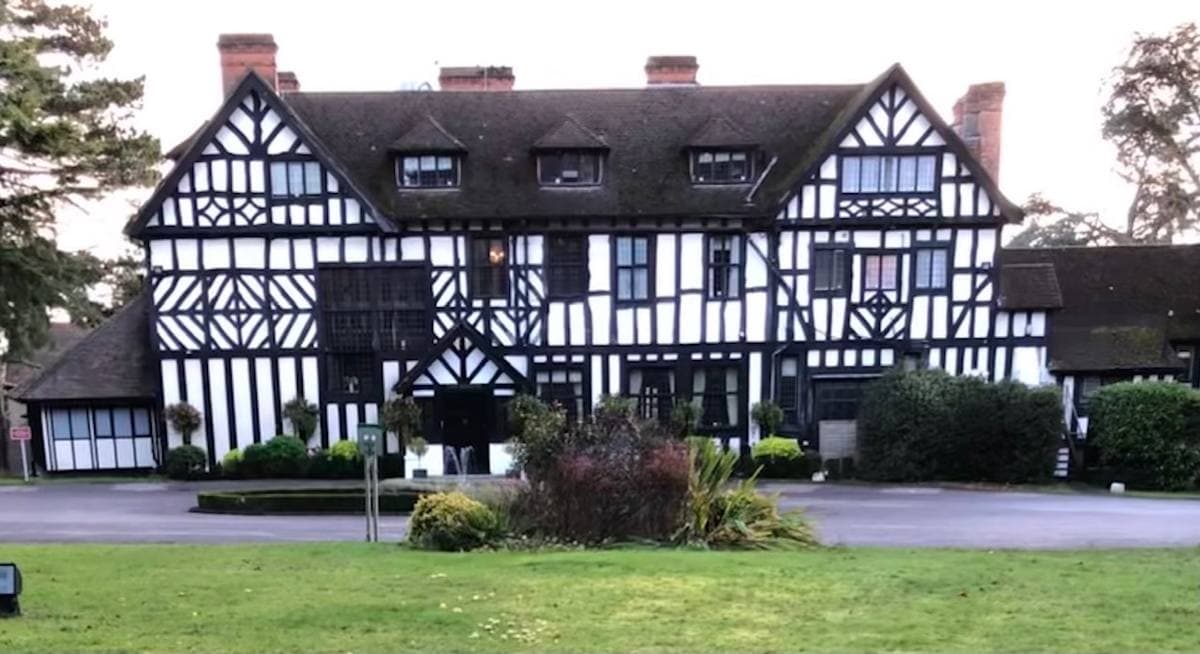 A black-and-white timbered Tudor-style house behind a lawn