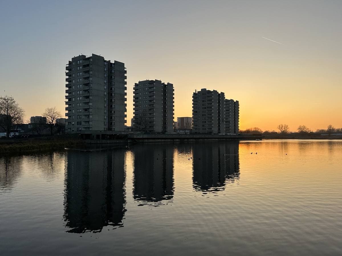 Three tower blocks reflected in a still lake under an orange evening sky