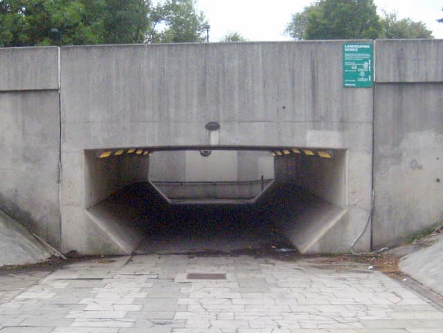 A low concrete pedestrian tunnel mouth set into a grey retaining wall
