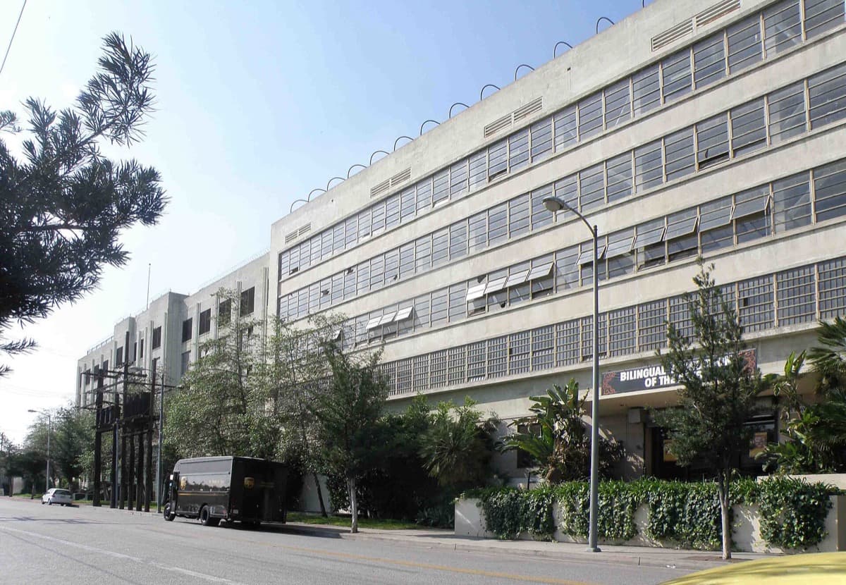 A long pale concrete building with rows of windows, seen from the street