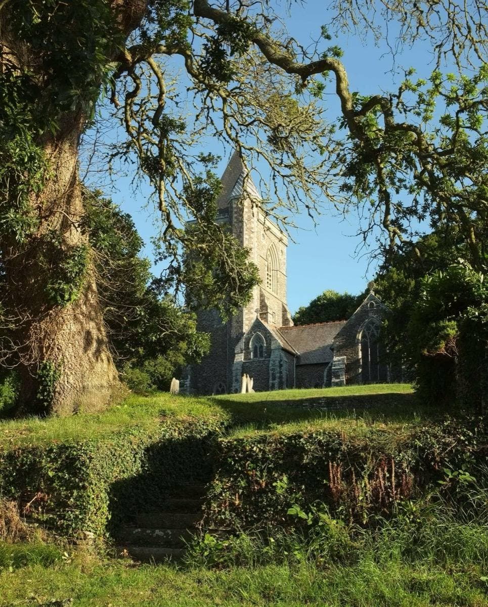 A grey stone church tower among trees