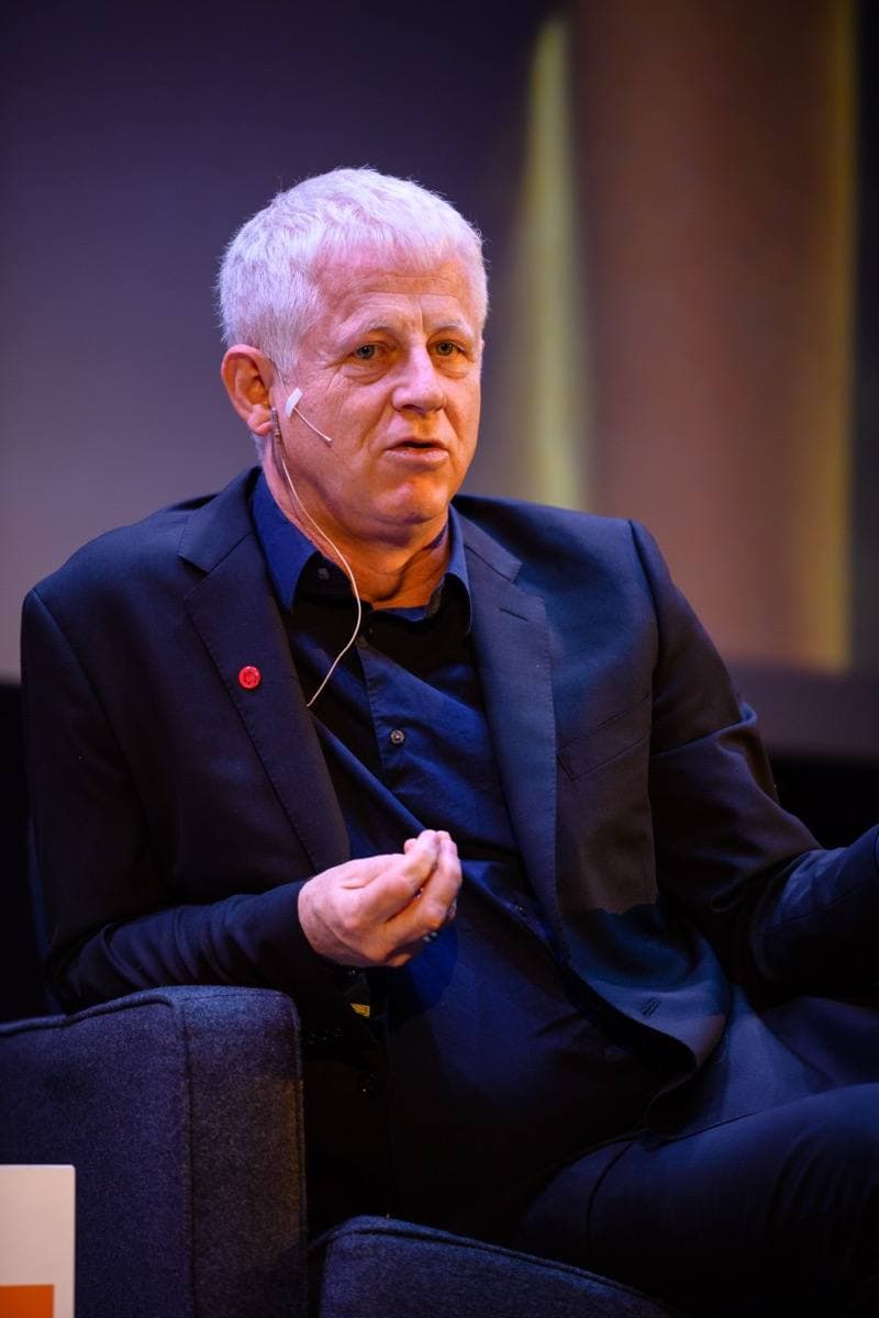 Richard Curtis, white-haired, in a navy jacket, talking on a stage