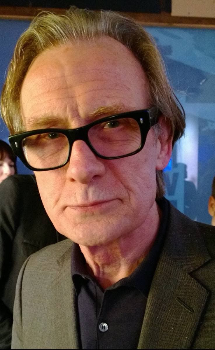 Bill Nighy in heavy black glasses and a grey jacket