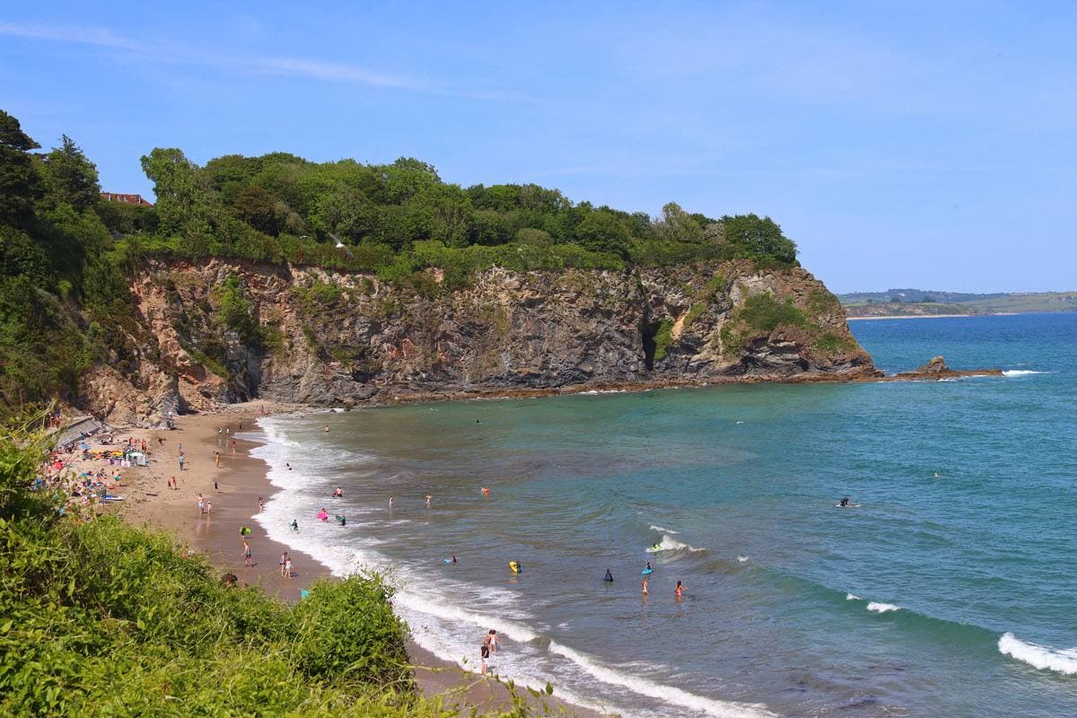 A small sandy cove under wooded cliffs, the sea bright blue