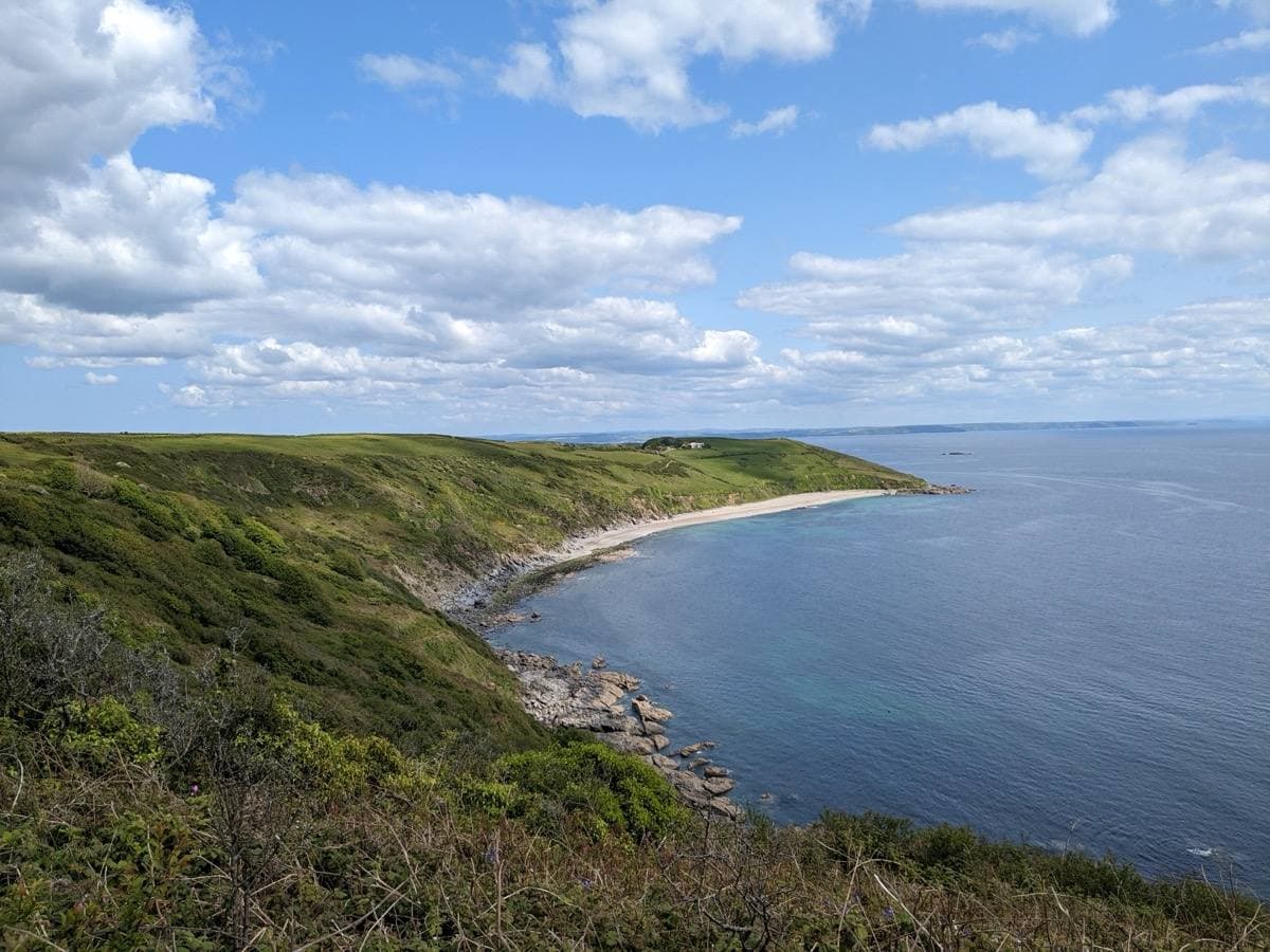 A long pale beach curving under green headland, seen from above