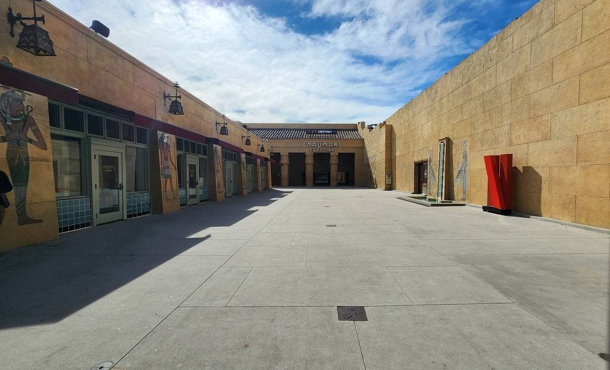 A long sunlit courtyard between ochre walls with painted Egyptian motifs