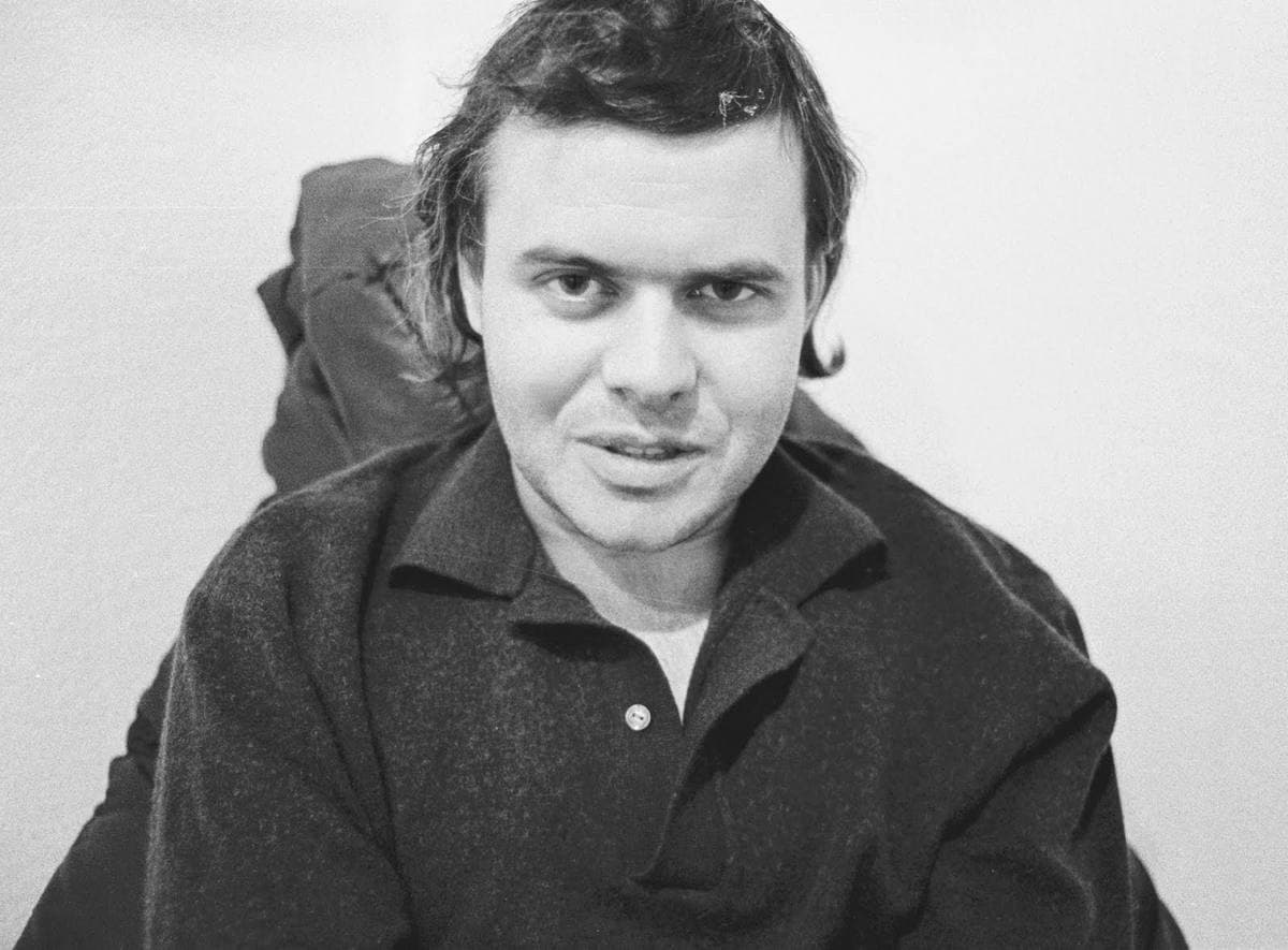H. R. Giger, dark hair falling to his collar, in a dark wool shirt, looking into the camera, black and white