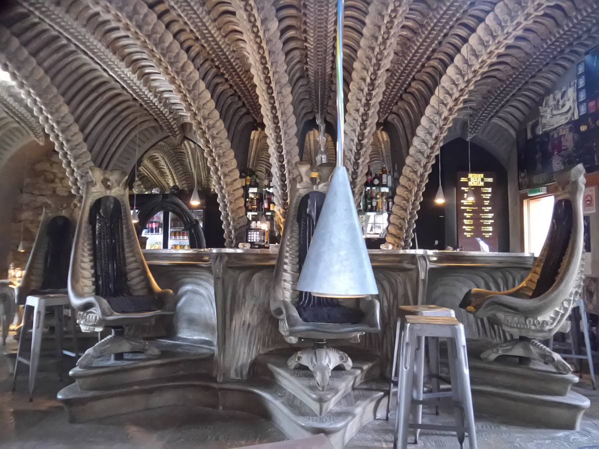 A vaulted bar of grey ribbed arches like a skeleton, with high-backed bony chairs