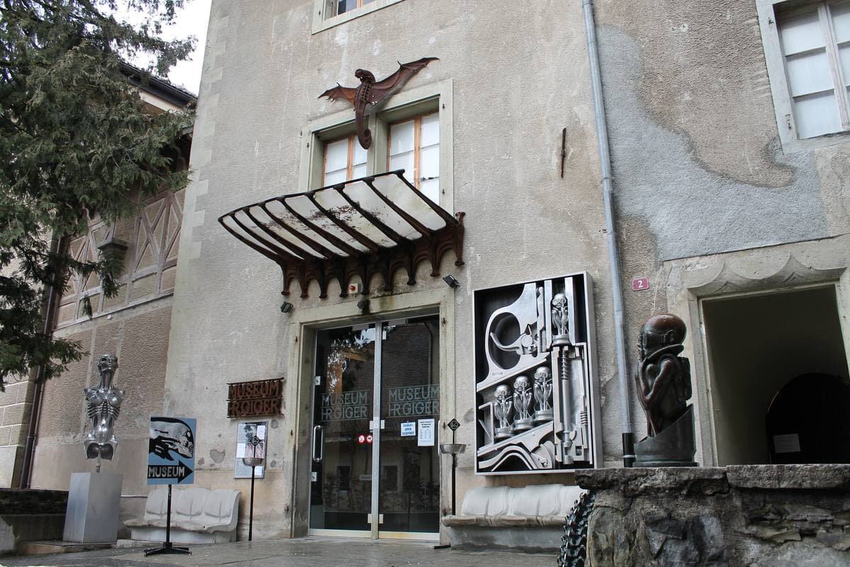 An old stone house front with metal sculptures and a winged figure over the door