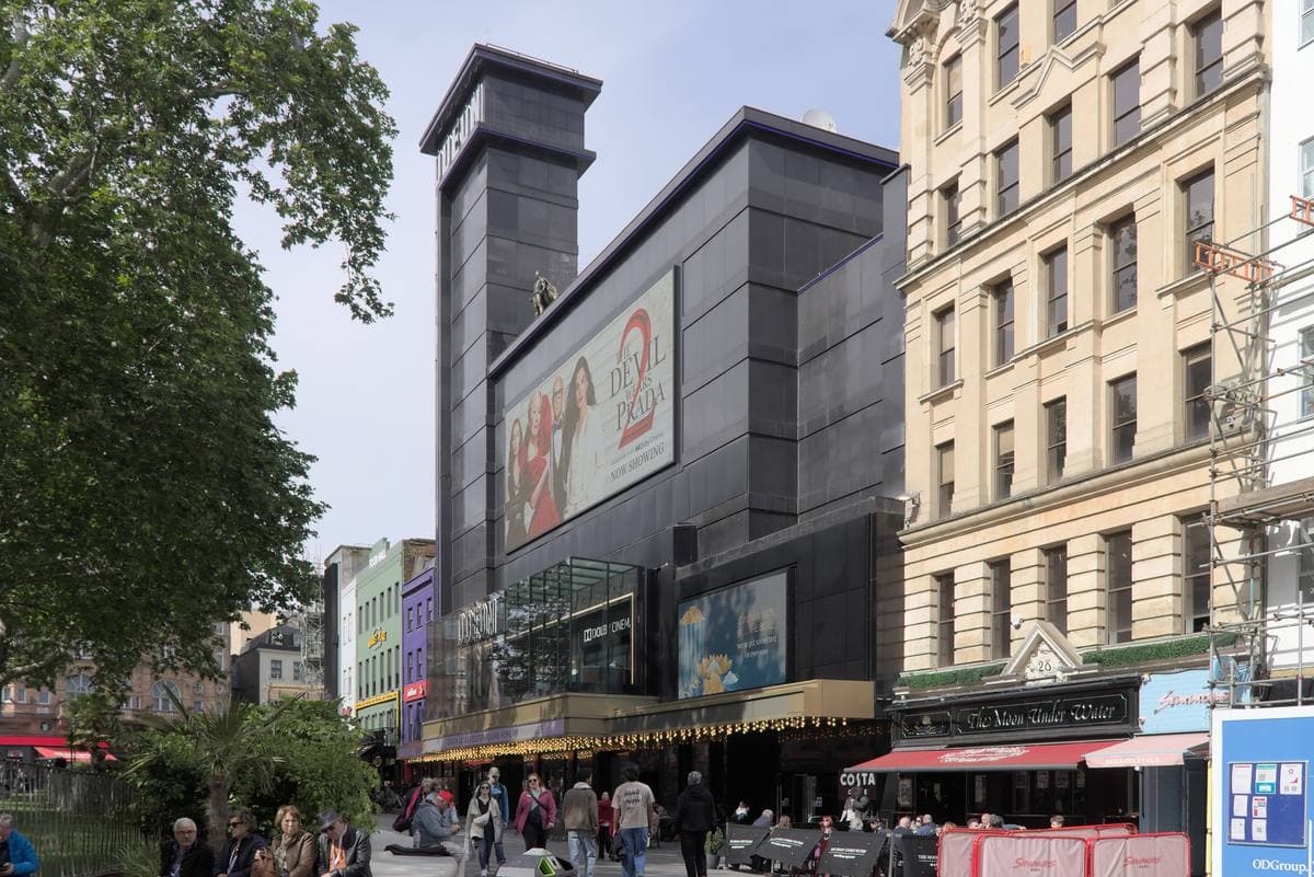 A tall black cinema front on Leicester Square with trees and people in front