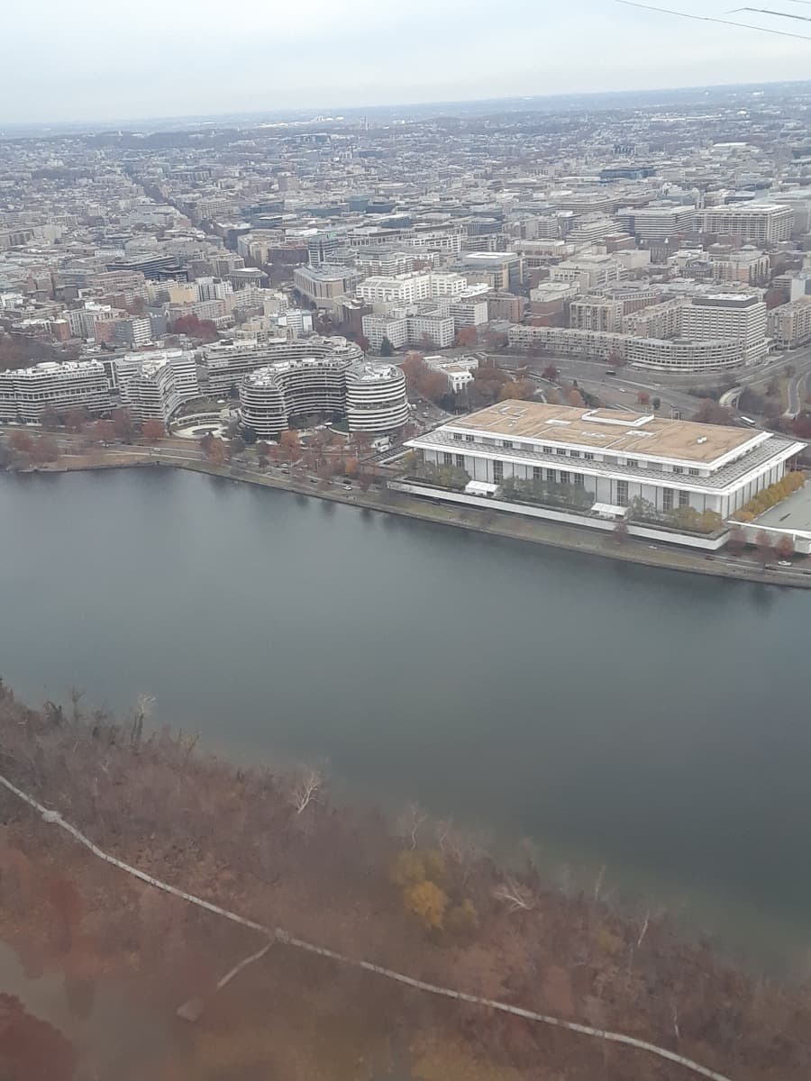 Aerial view of a long white building and a curved apartment complex on a riverbank