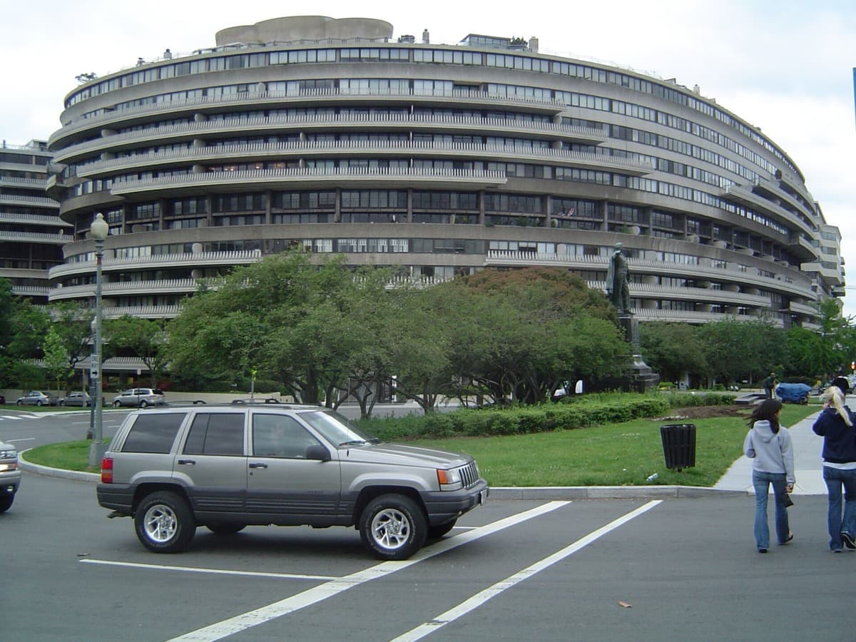 A curved cream-coloured apartment and office block with balconies, seen across a lawn