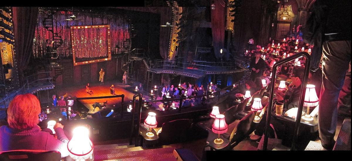 A theatre laid out as a nightclub, red table lamps glowing in the dark