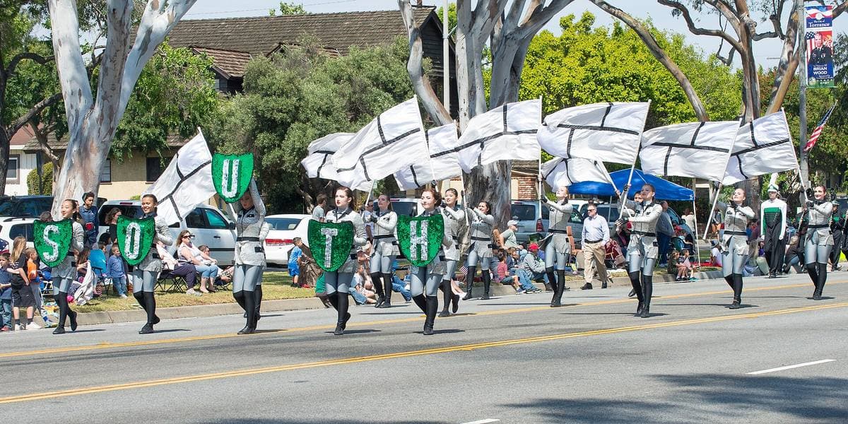 A high-school marching band in green and white uniforms parading down a street