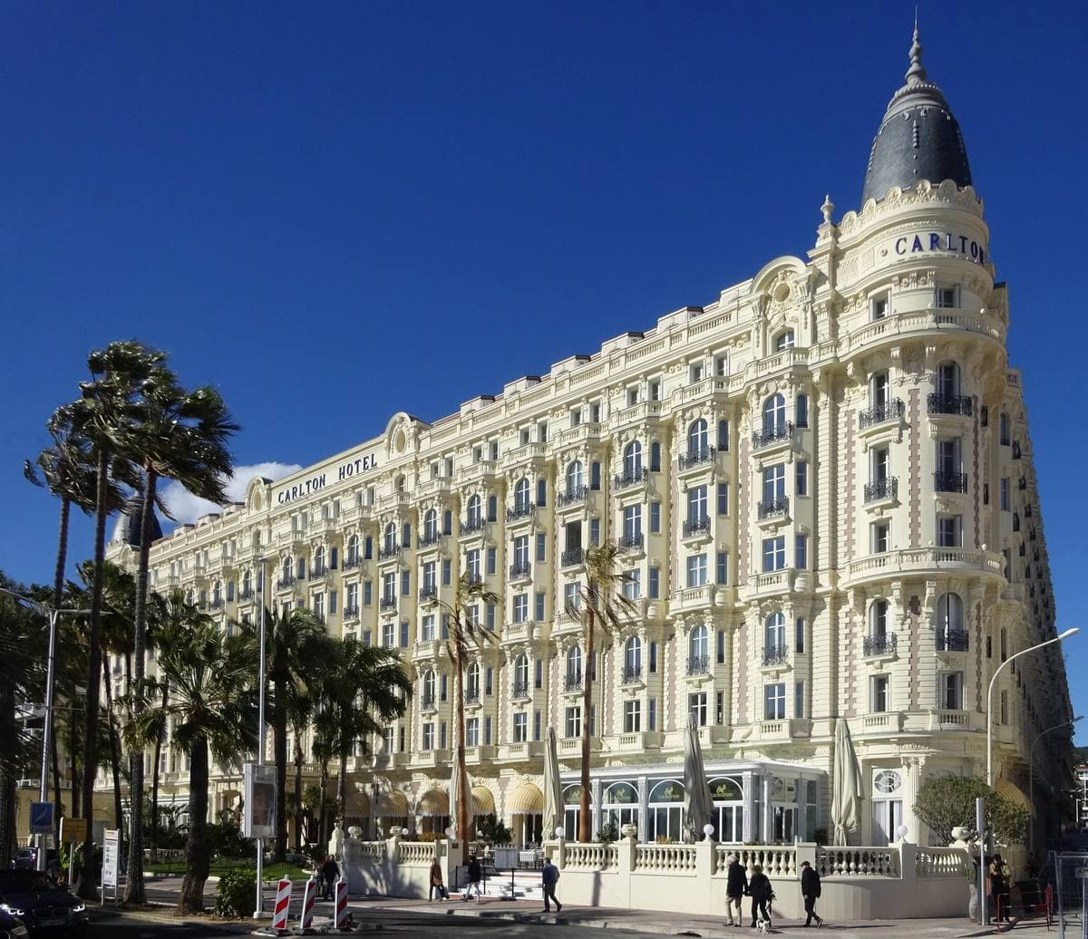 A long white seafront hotel with two domed corner towers and palm trees