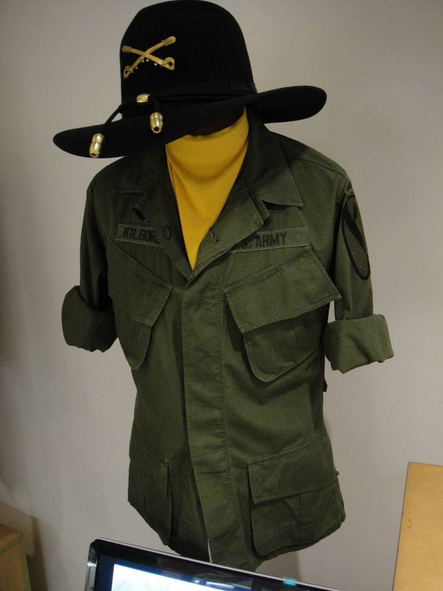 An olive combat shirt with a yellow scarf on a mannequin