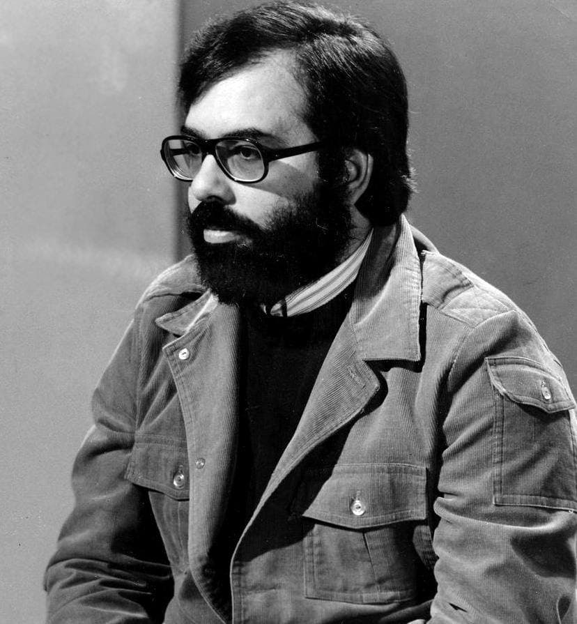 Francis Ford Coppola, bearded, in heavy-rimmed glasses and a work jacket, looking to one side