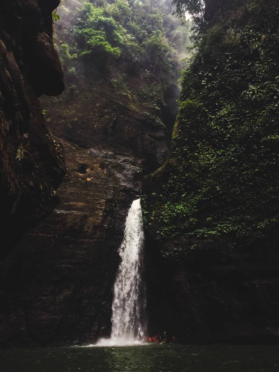 A tall waterfall dropping into a green pool between jungle cliffs
