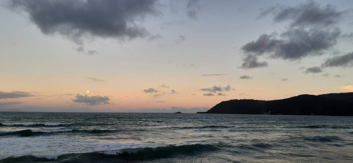 Surf rolling onto a wide beach with green headlands behind