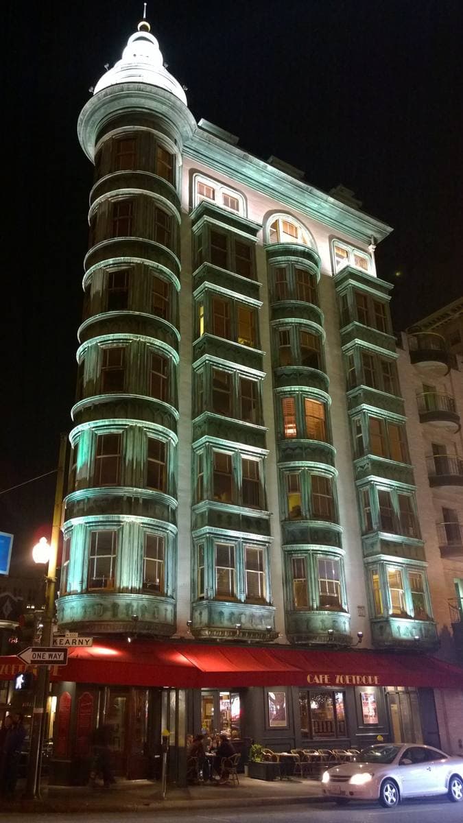 A narrow green copper-clad flatiron building on a street corner