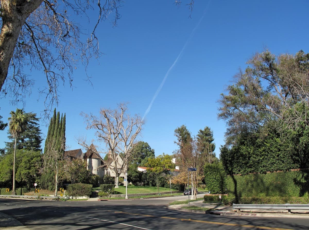 A quiet residential street lined with trees and period-revival houses