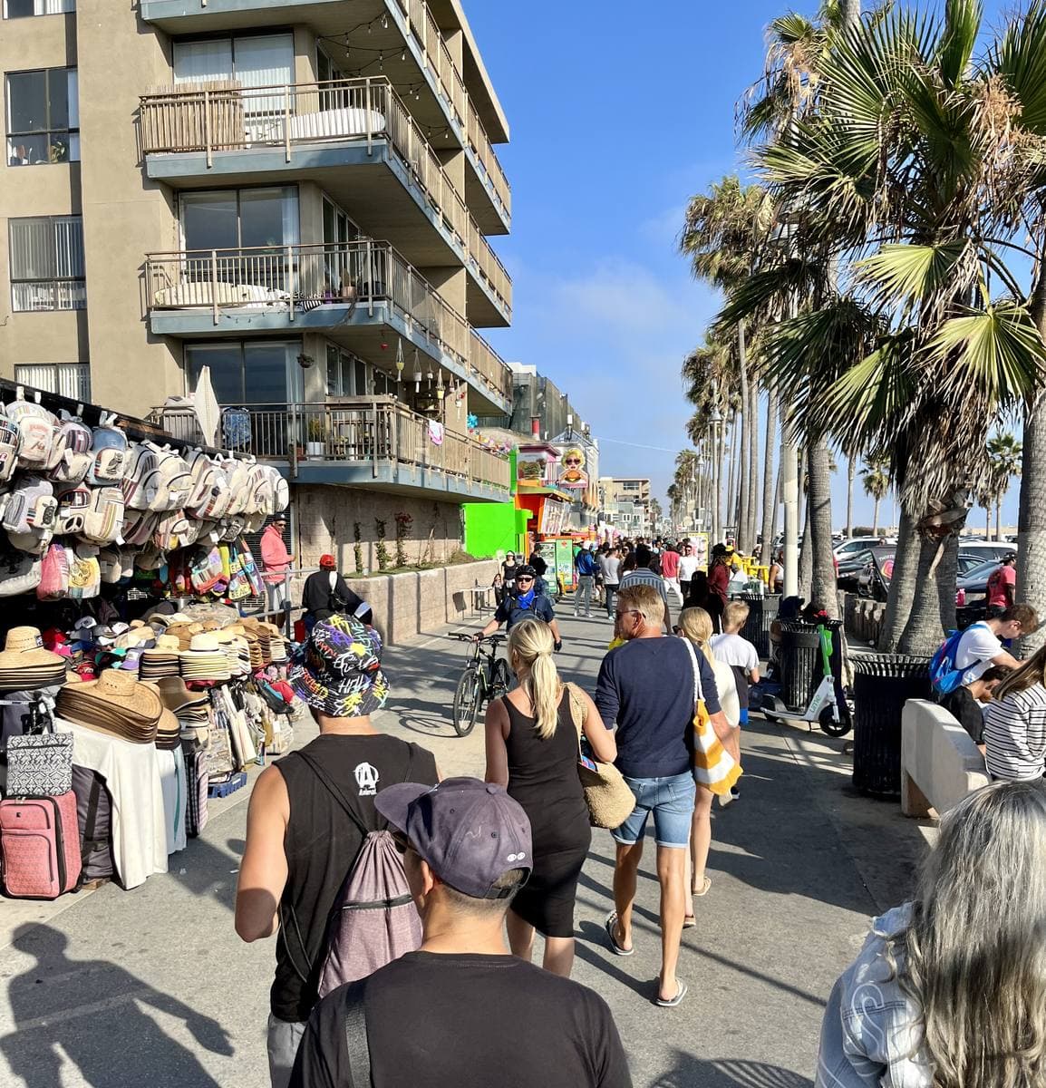 A busy palm-lined boardwalk with stalls and low apartment blocks on a sunny day
