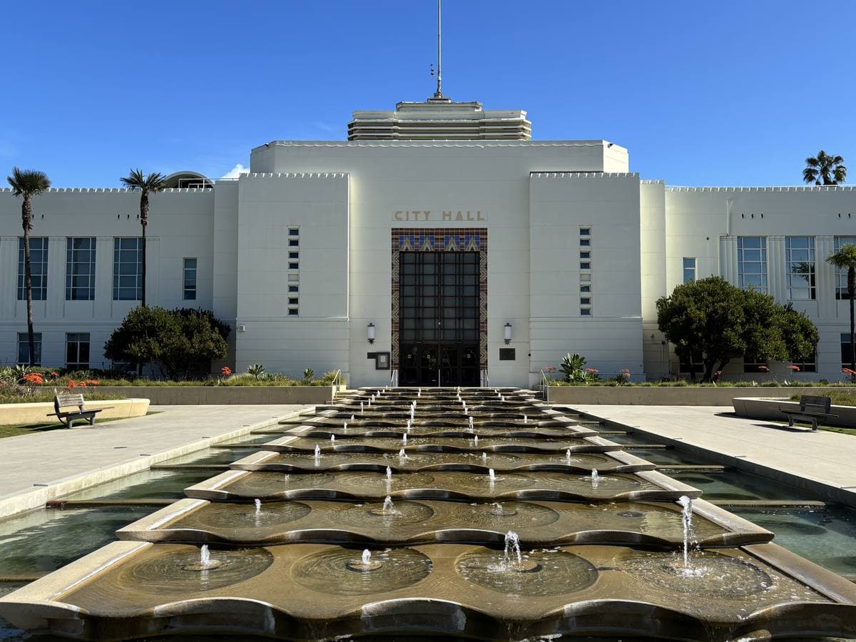A white Art Deco civic building with a central tower behind a long stepped fountain