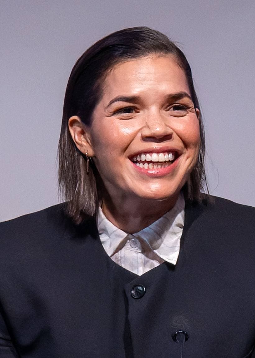 America Ferrera laughing, in a dark jacket and white collar