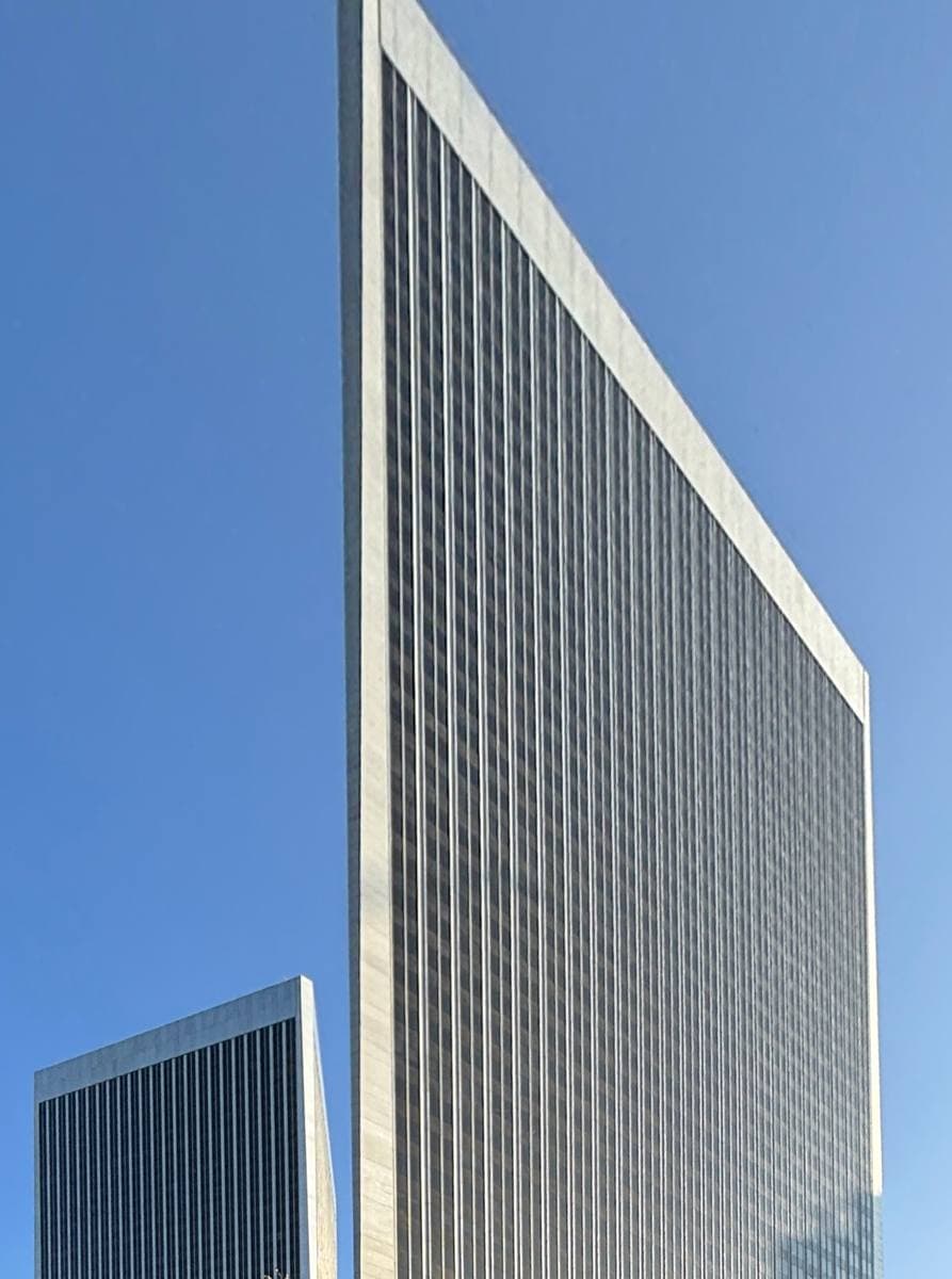 A tall silver office tower with fine vertical ribs against blue sky