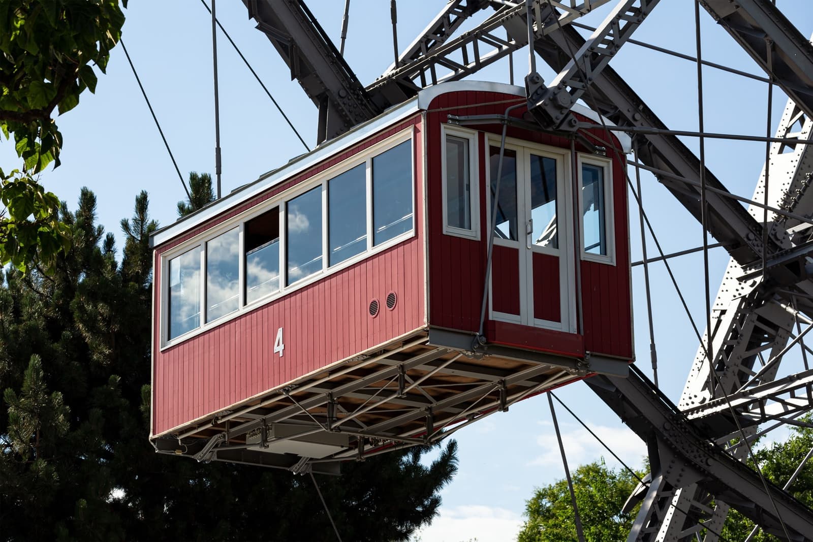 A red wooden Ferris-wheel cabin, numbered 4, hanging from the wheel’s iron spokes