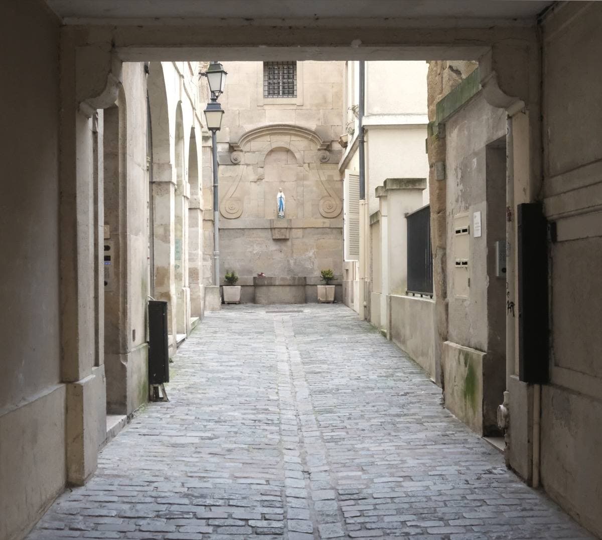 A narrow paved lane turning a corner between pale walls