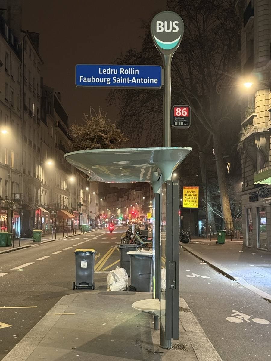 A street at night under lamps, with a bus stop sign