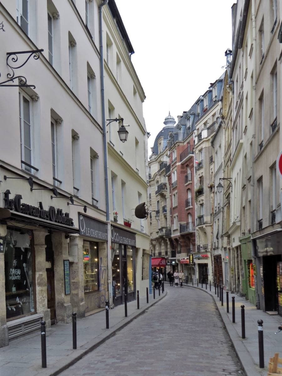 A narrow street of old houses and shopfronts, with bollards along the pavement