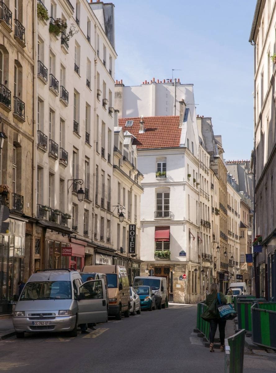 A street of tall Paris houses with shops and parked cars