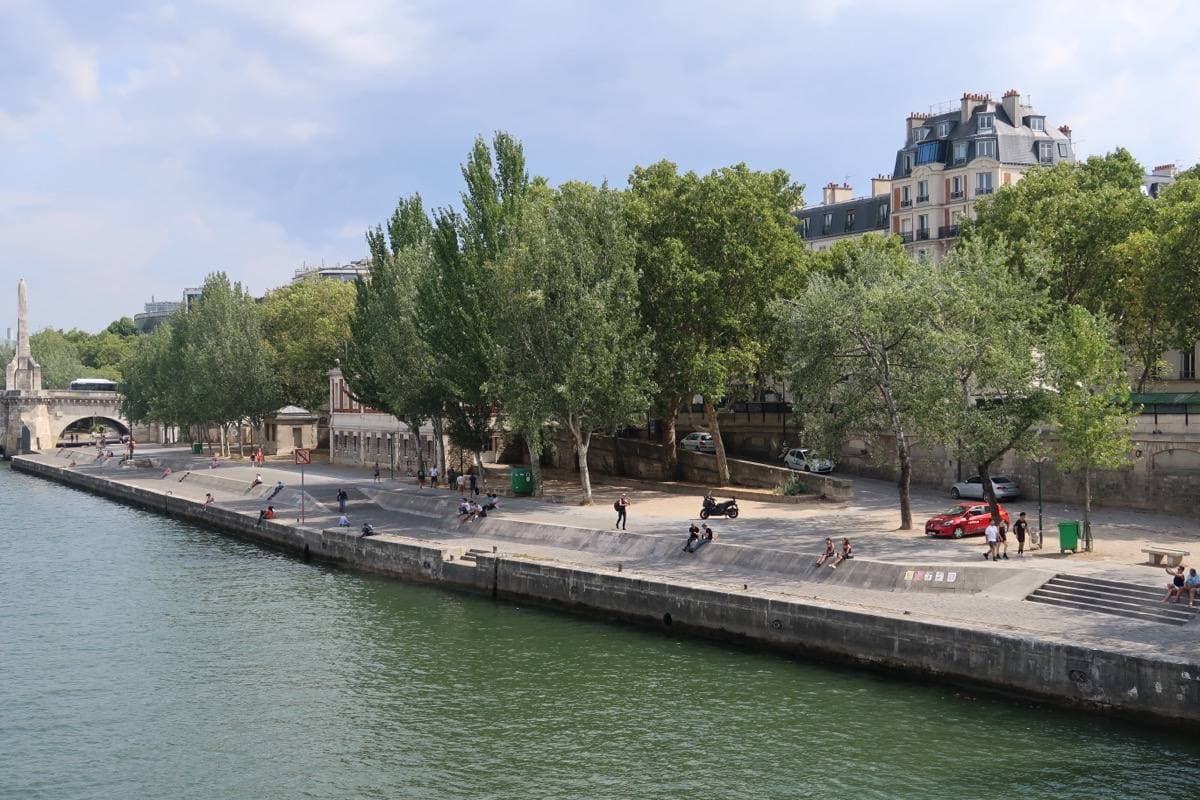 A stone quay along the Seine with tall trees, seen from across the water