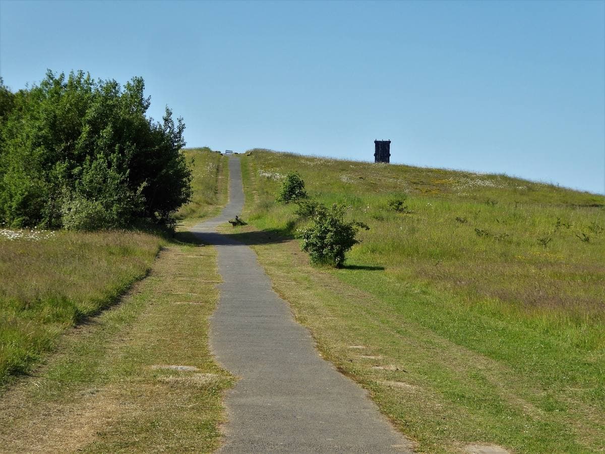 A tarmac path climbing a grassy hill to a pit cage on the top