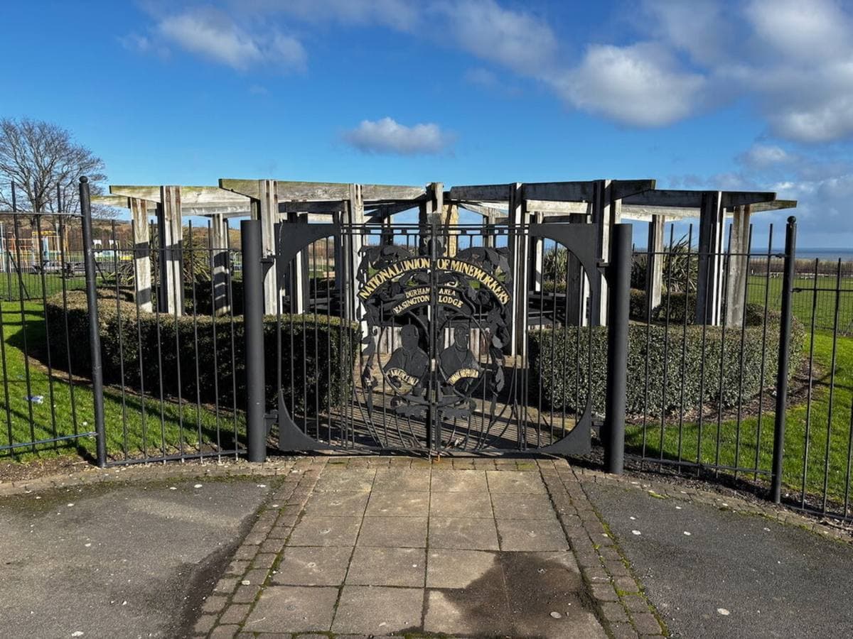 A memorial garden behind iron gates, with a timber pergola round it