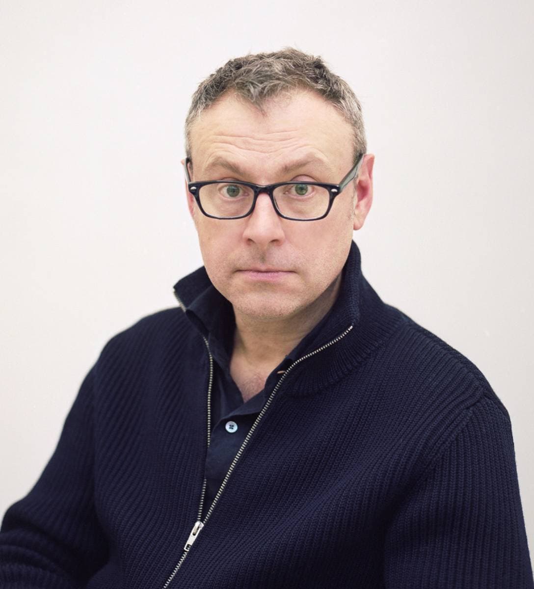 Lee Hall in glasses and a navy jumper against a white wall