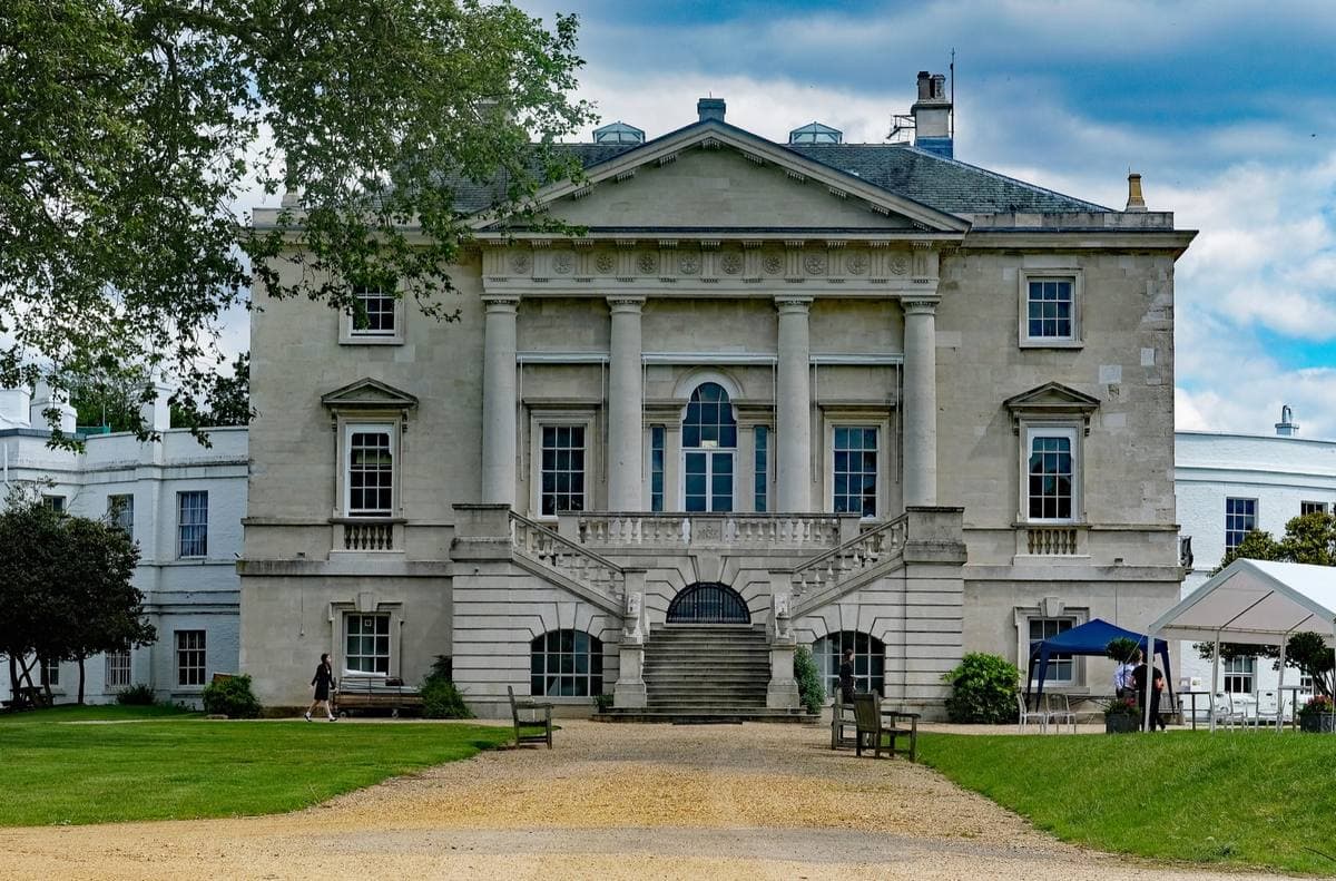 A pale Palladian house with a portico at the end of a gravel drive