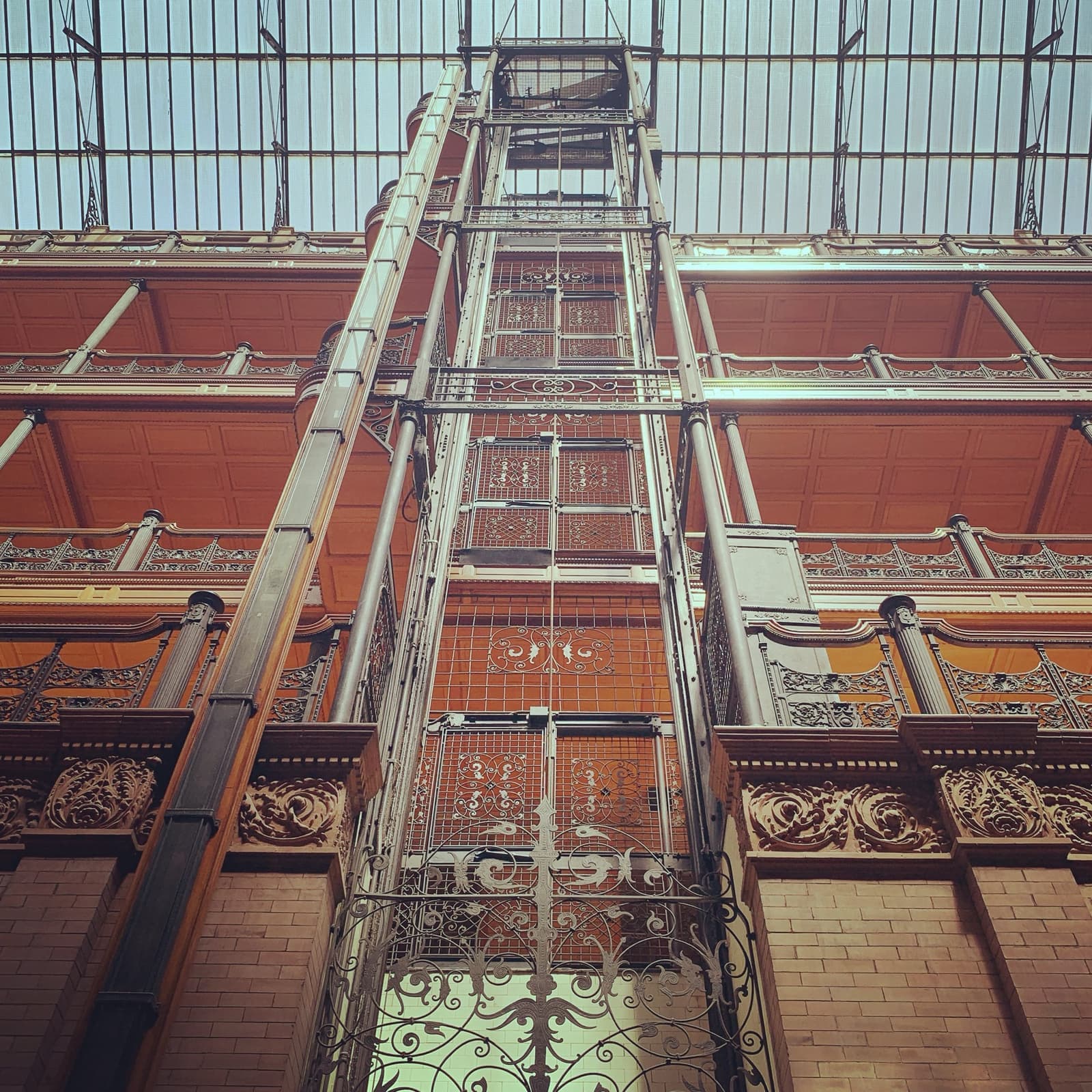 Looking up an open iron lift cage to a glass roof