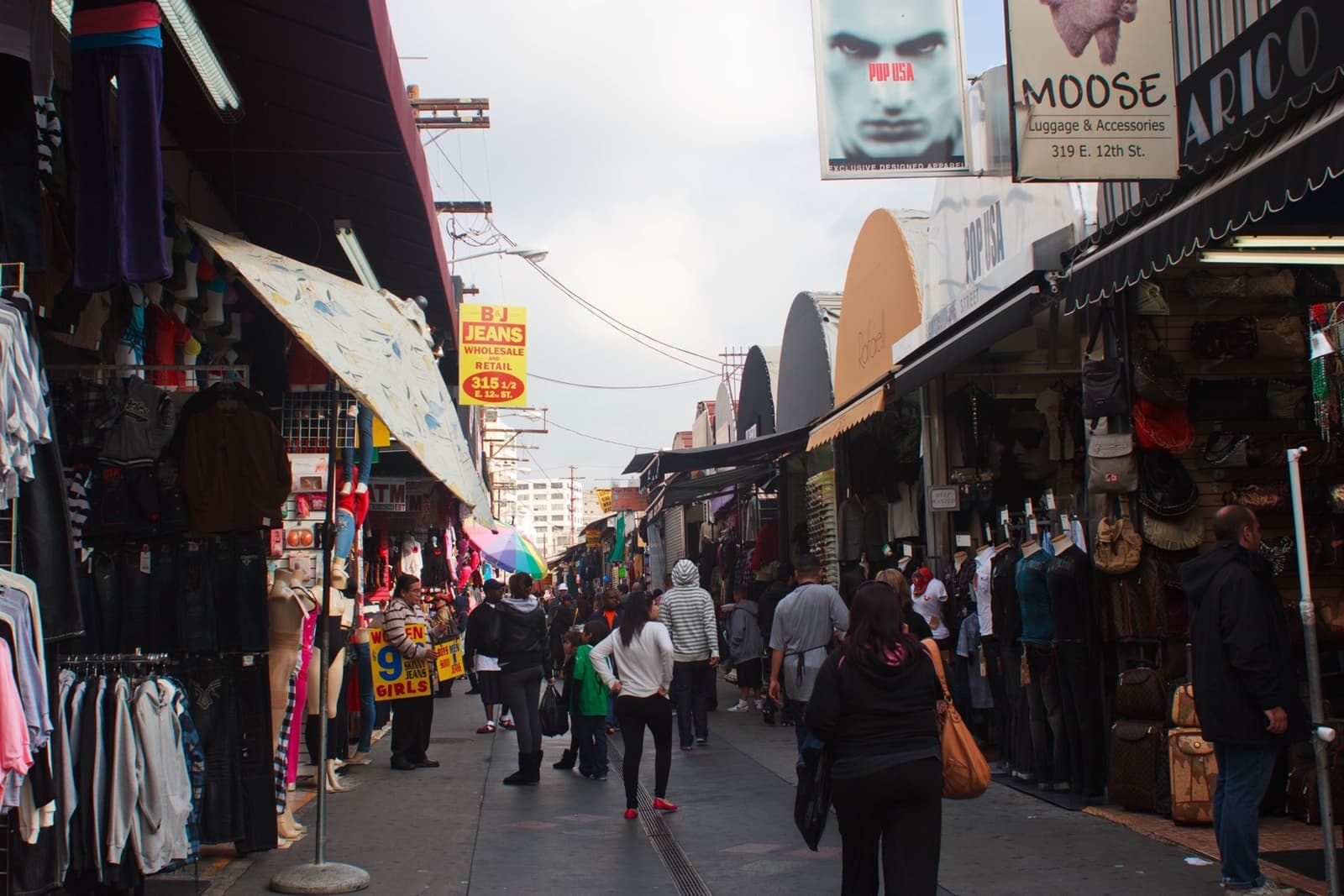 A narrow alley crowded with shoppers between stalls hung with clothes