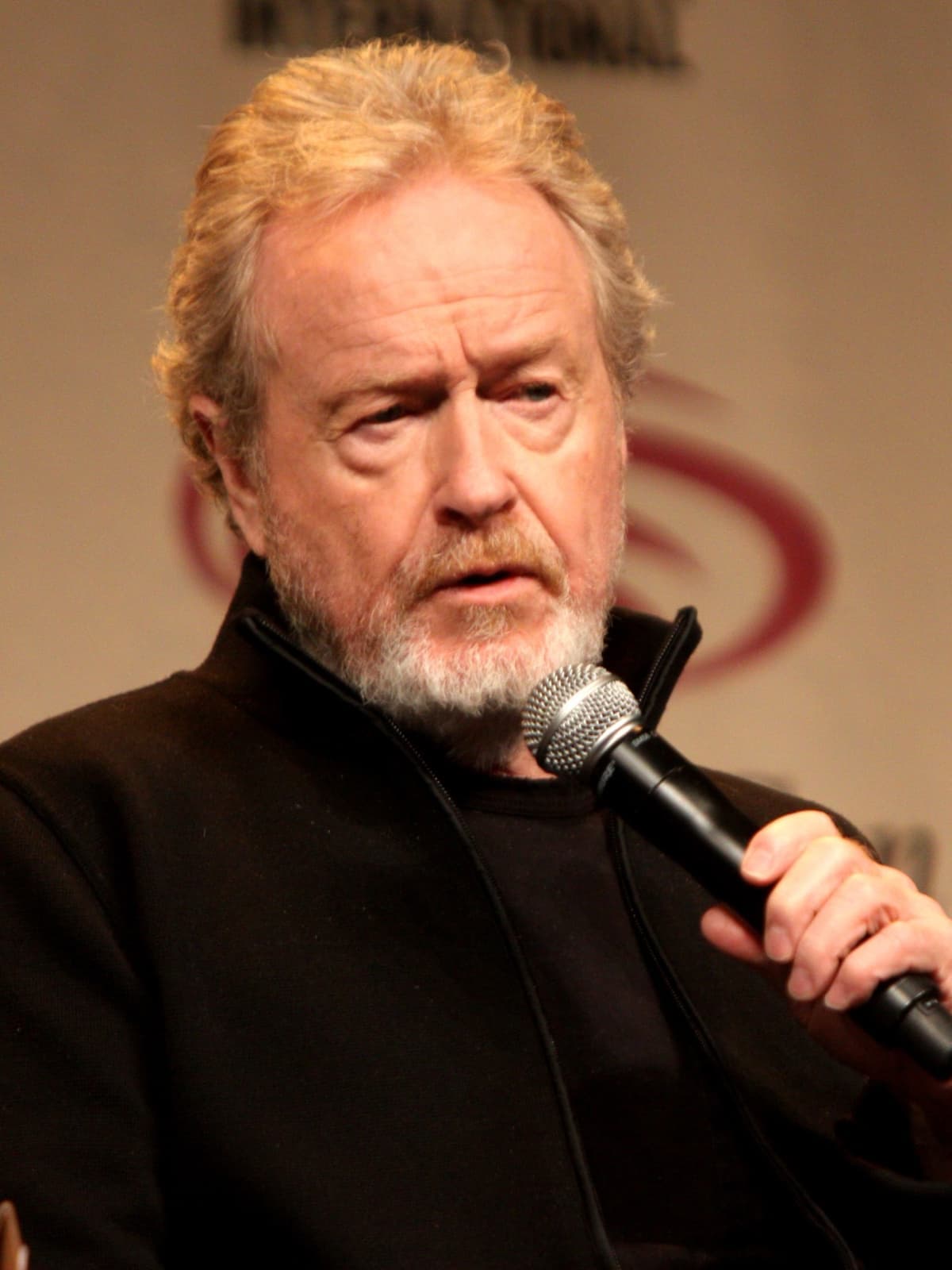 Ridley Scott, grey-bearded, speaking into a microphone