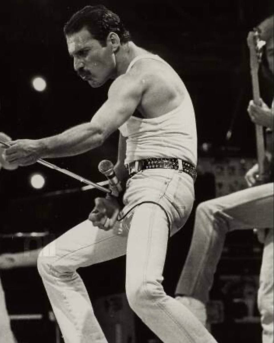 Freddie Mercury singing at Live Aid in a white vest, microphone raised