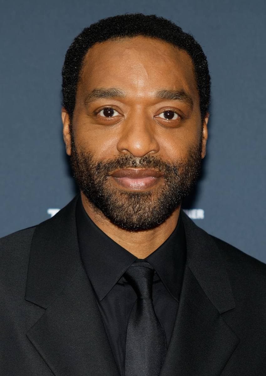 A bearded man in a black suit and tie, smiling slightly