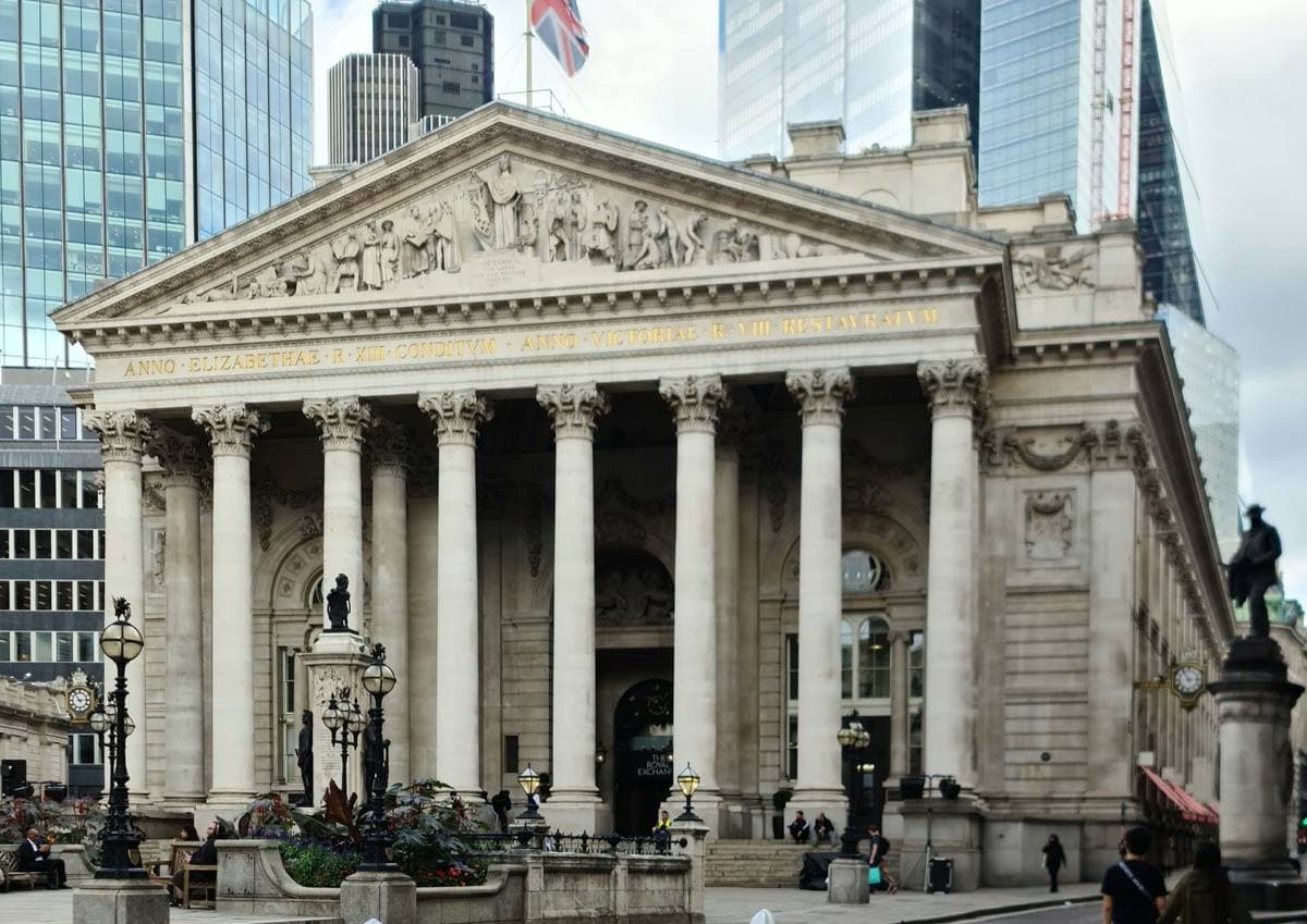 A Classical stone portico with eight columns and a carved pediment, with City towers behind
