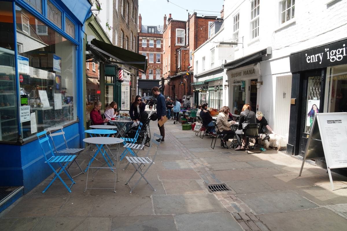 A narrow pedestrian lane with café tables and blue chairs outside small shopfronts