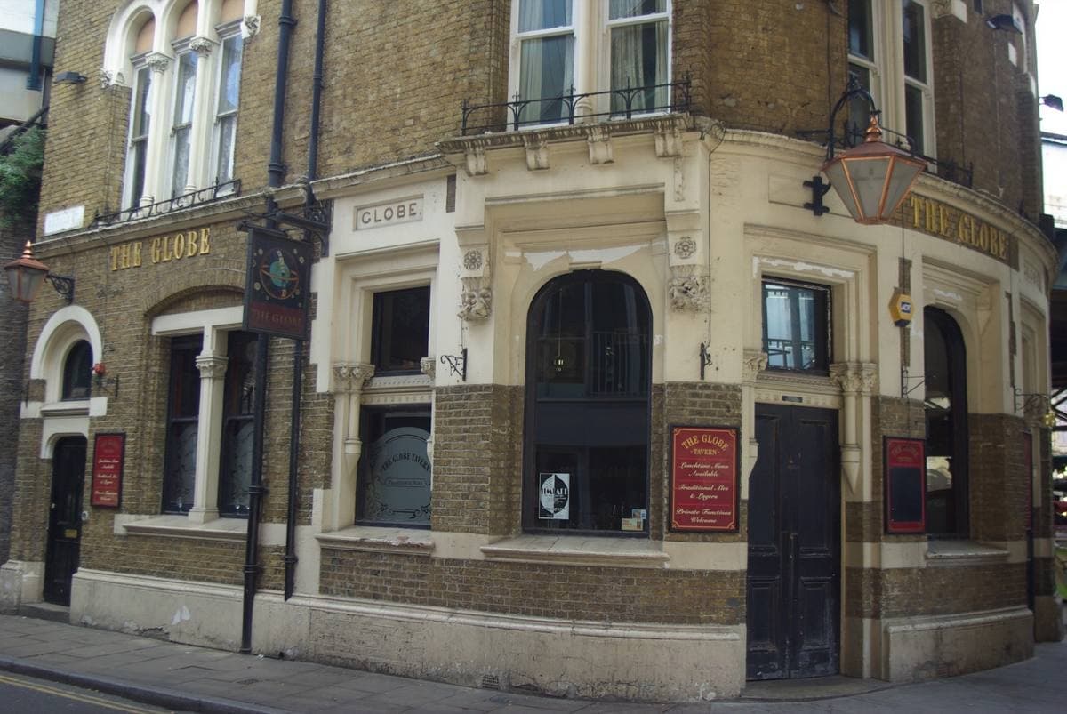 A curved brick and stone Victorian pub front with arched windows and gold lettering reading The Globe